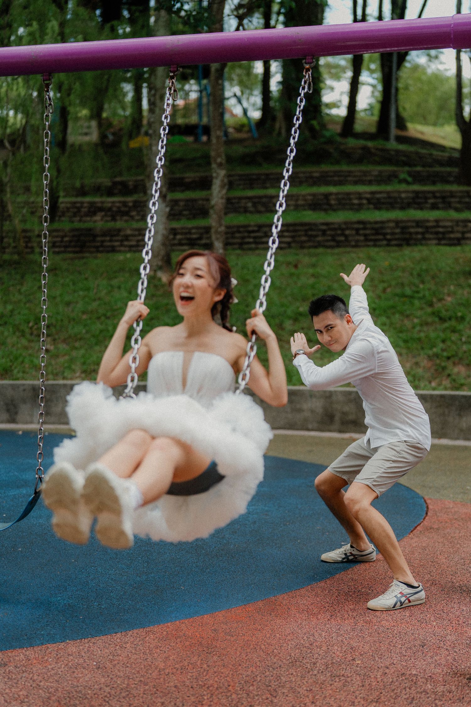 Couple enjoying a carefree moment at a playground as one pushes the other on a swing with joyful expressions.