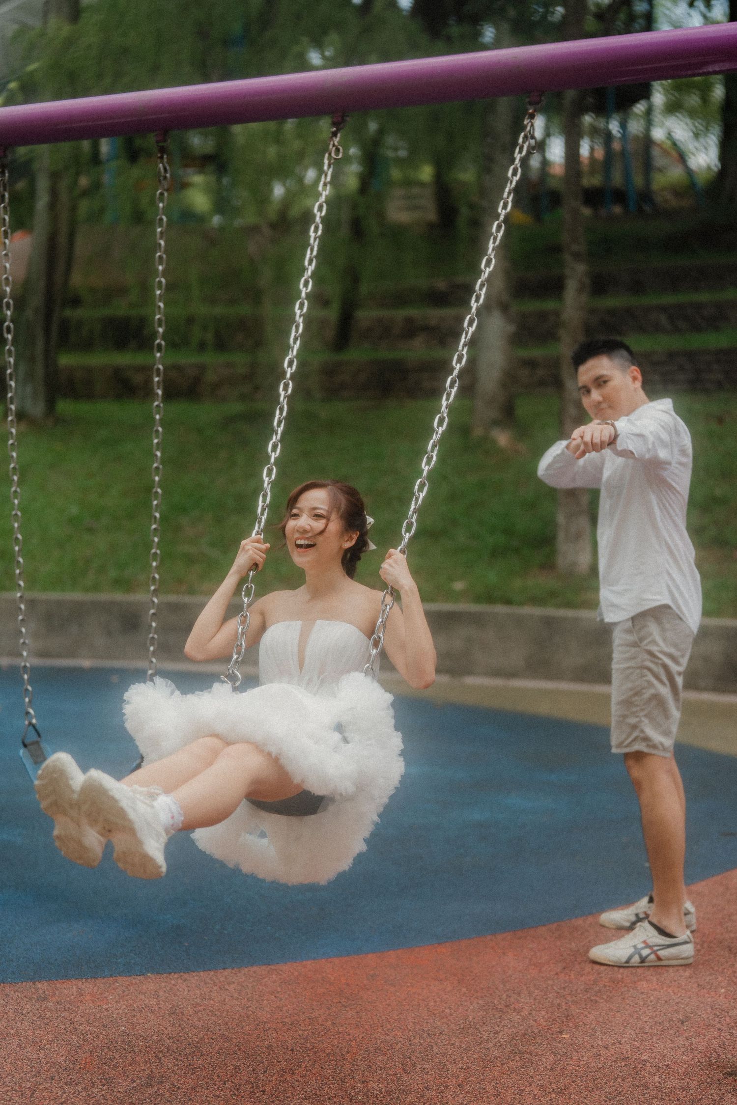 Couple enjoying swings at a park with blue and red ground surfacing.
