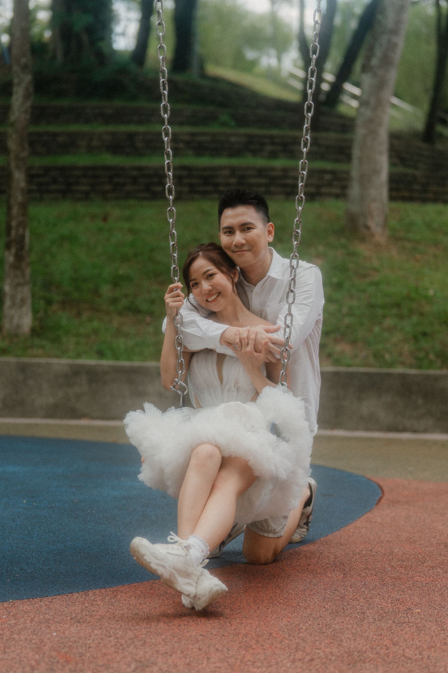 A couple sharing romantic moments while sitting together on a playground swing at a park.