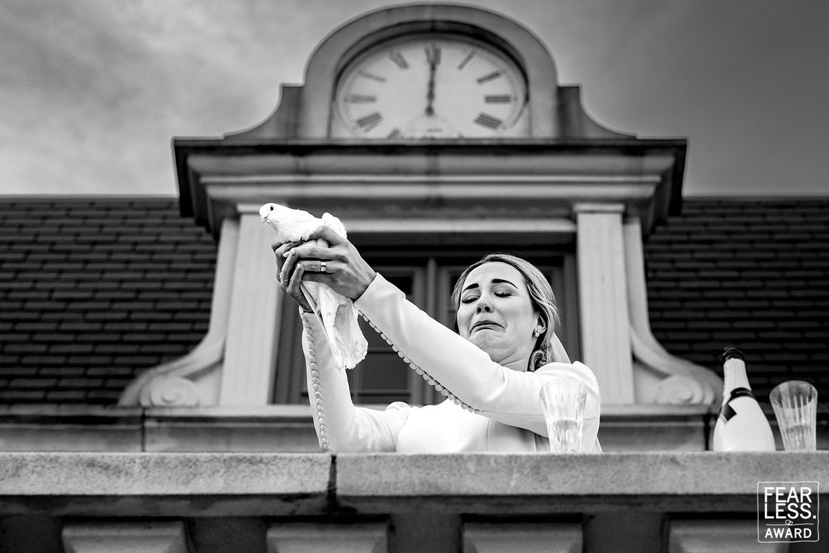 A black and white photograph captures a joyful moment on a balcony beneath a clock tower at a historic building.