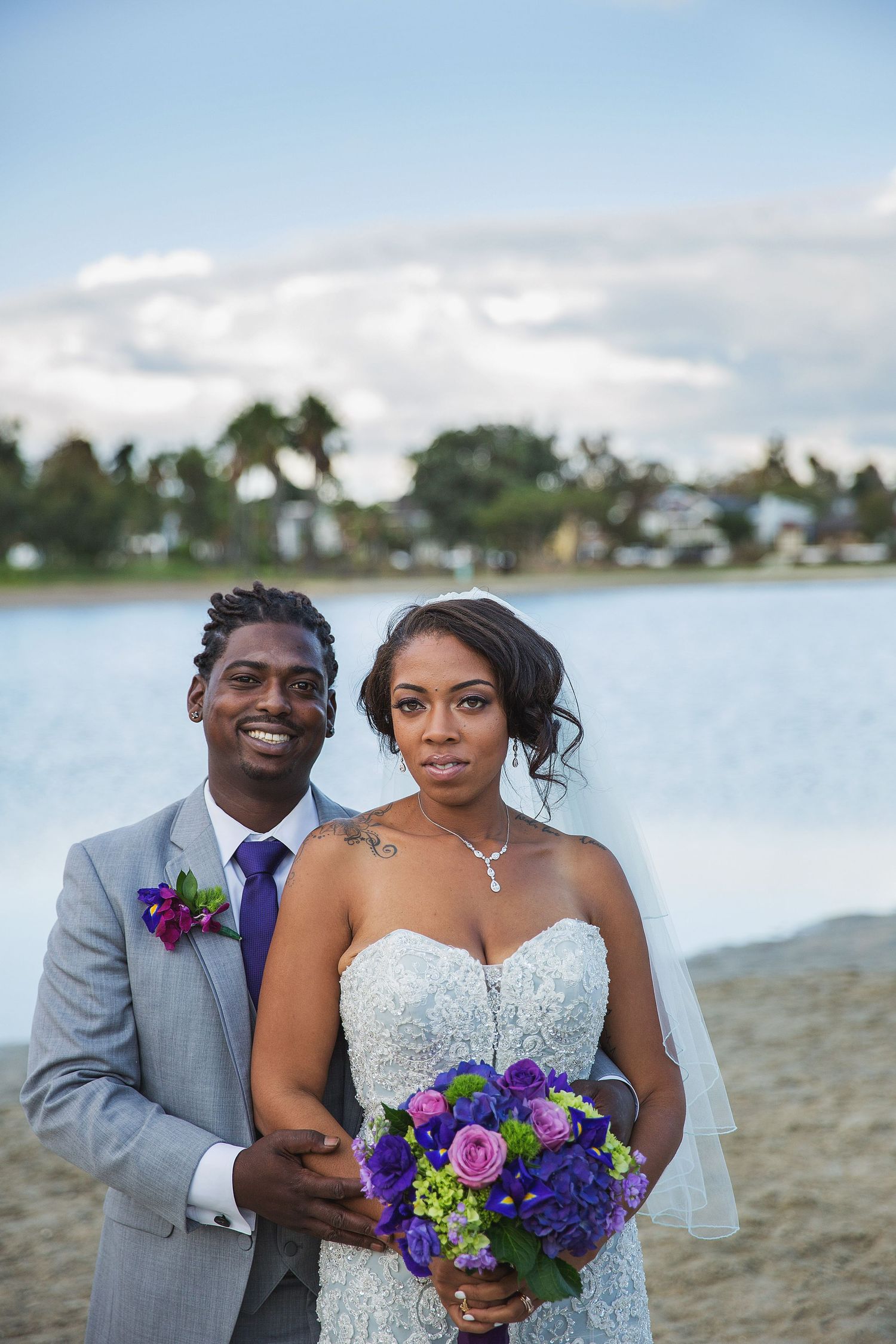 A beach wedding ceremony with vibrant purple and green floral bouquet against a tropical waterfront backdrop.