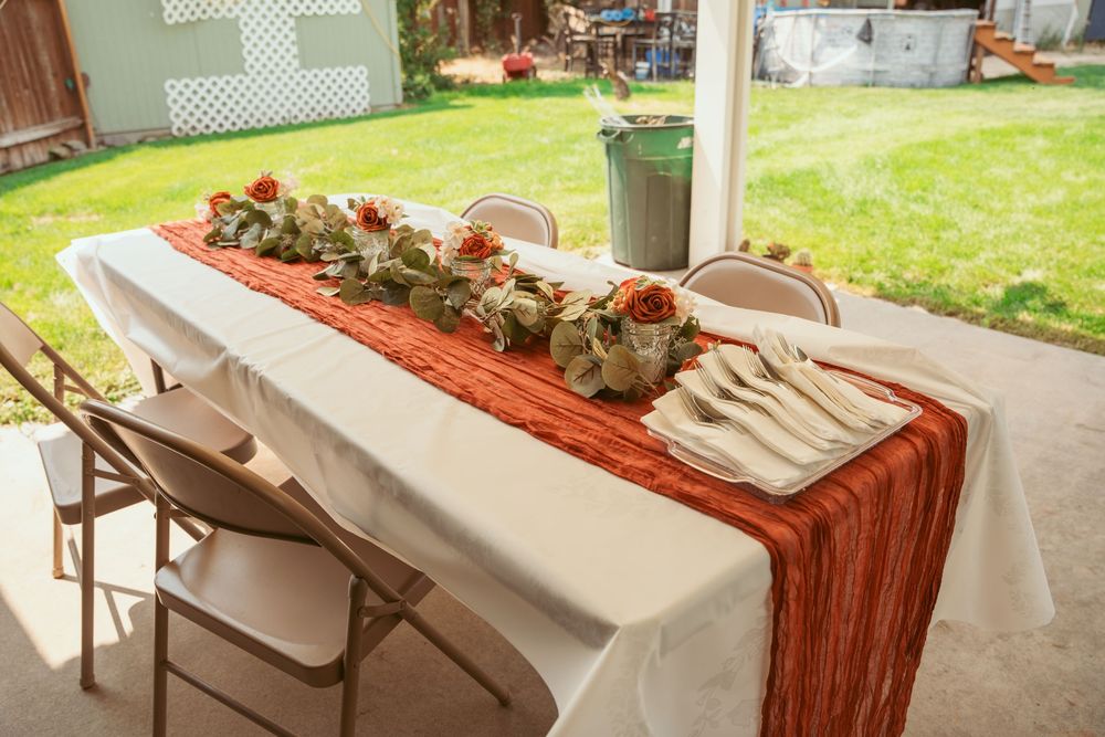A decorated banquet table with white tablecloth and burnt orange runner features potted plant centerpieces.