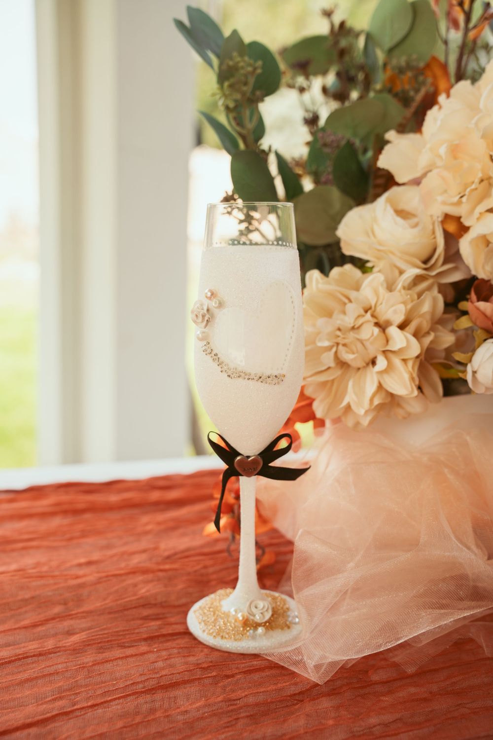 Decorated champagne flute with peach florals and tulle on red tablecloth.