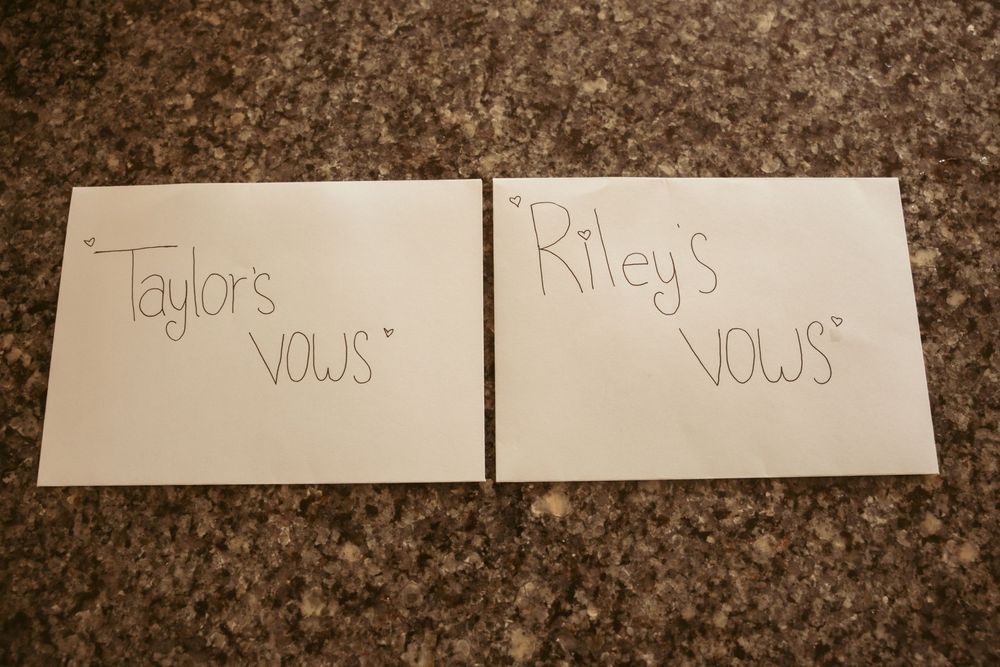 Two handwritten wedding vow books labeled 'Taylor's Vows' and 'Riley's Vows' on granite countertop.