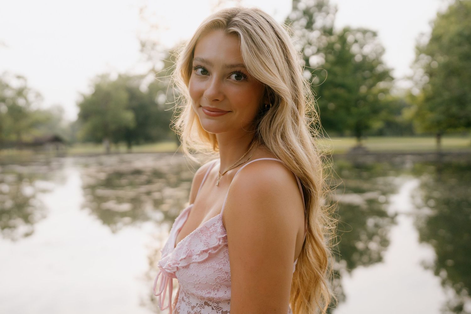 Someone wearing denim shorts and a white lace top poses by a stone wall near a lake on a sunny summer day.