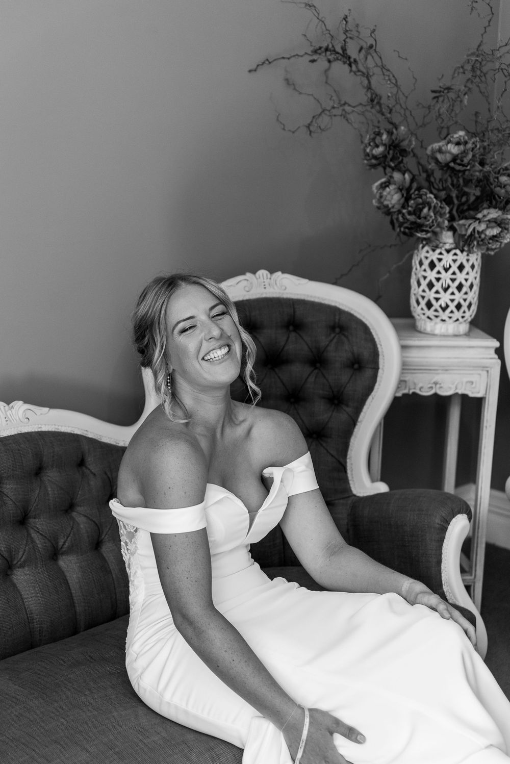 A series of black and white photos showing someone laughing while lounging on an elegant tufted couch with white ornate chairs.