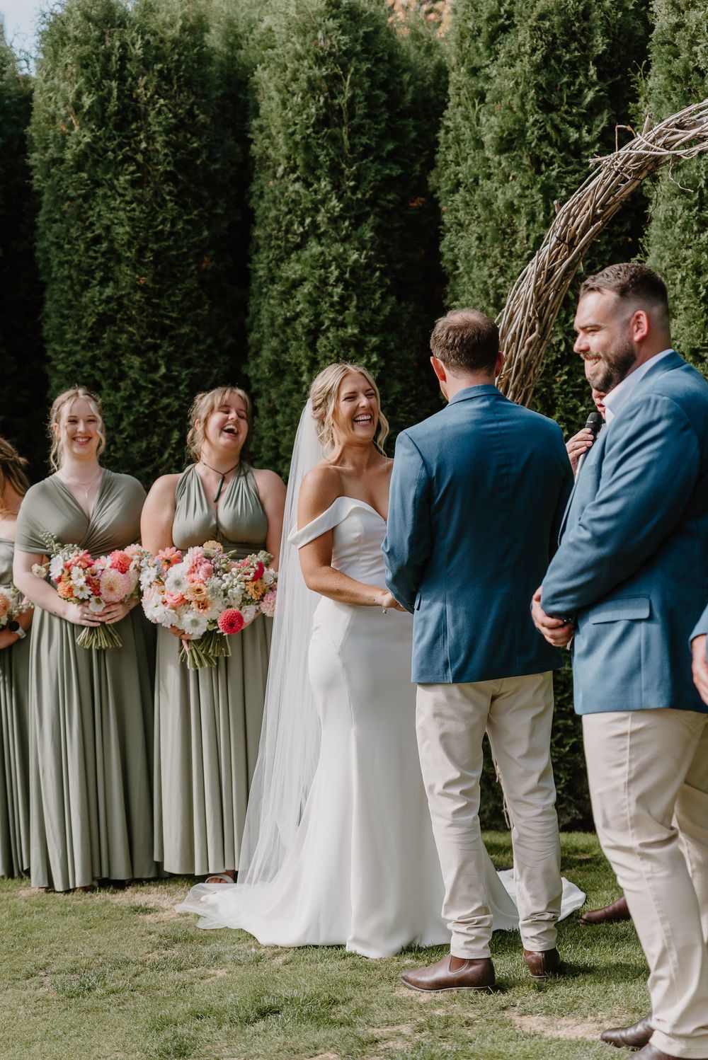 Wedding party lines up on lawn with bridesmaids in sage dresses and groomsmen in navy and khaki attire.