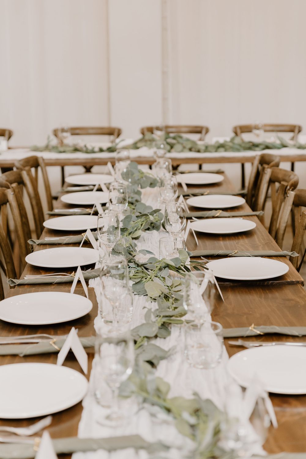 Long wooden dining table set with white plates and delicate eucalyptus garland for an elegant wedding reception.