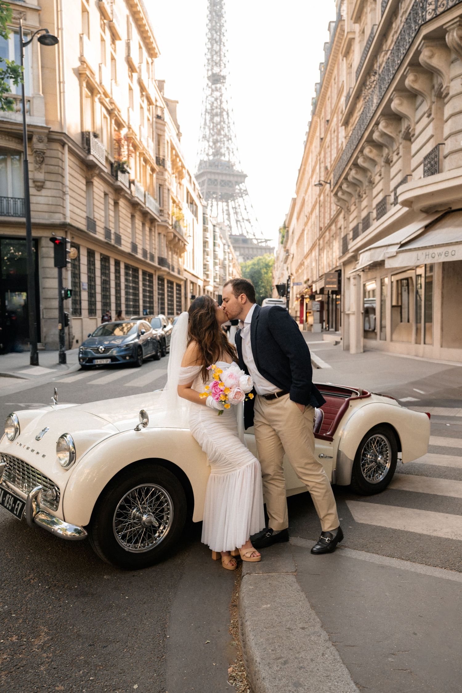 Stylish couple poses under arched colonnade with palm trees visible in background, captured in black and white.