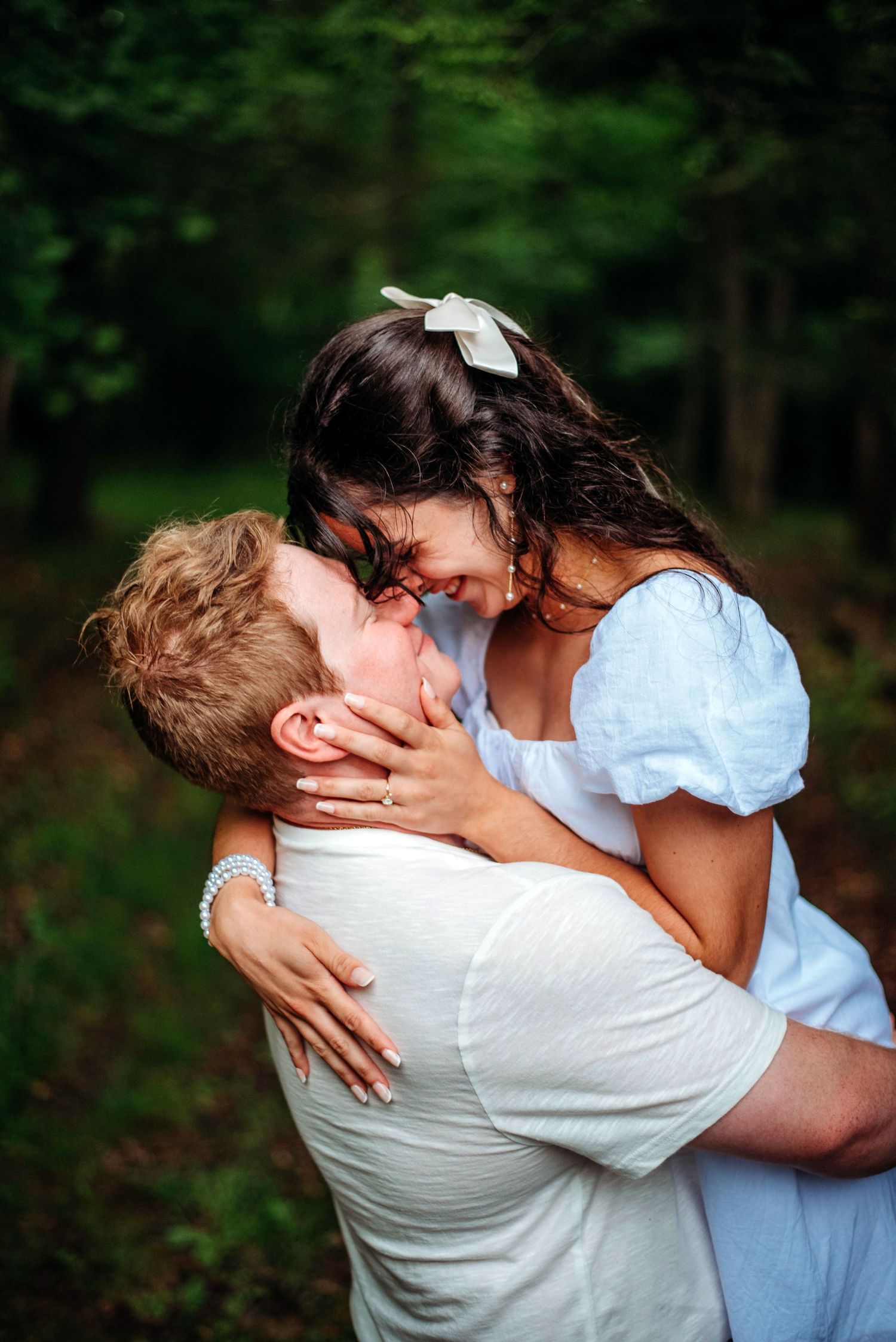 A couple in white clothes embraces in a tender moment in a forest setting. Engagement photos in VA.