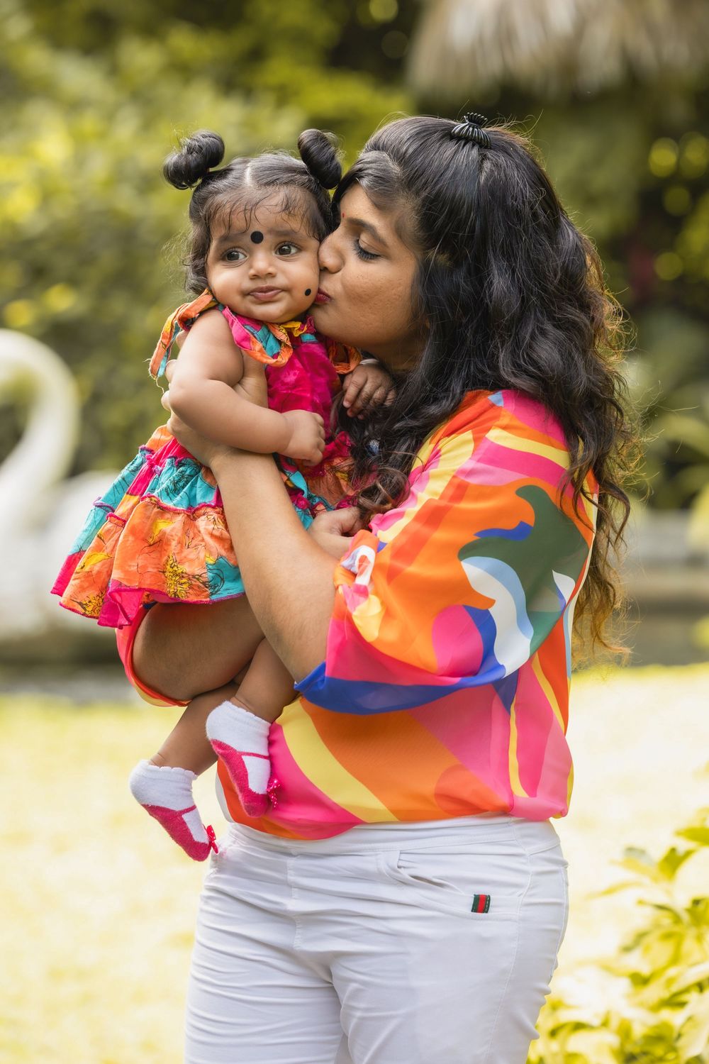 A tender outdoor family moment showing vibrant colorful outfits and affection in a sunny garden setting.