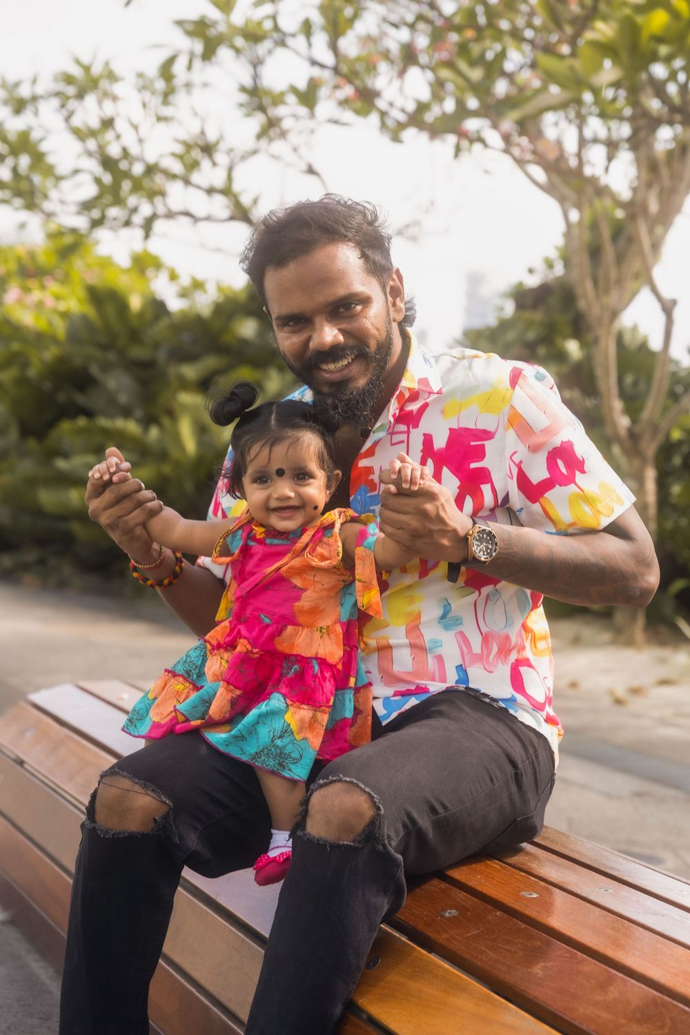 A happy family moment captured on a wooden bench in a garden setting with vibrant tie-dye shirts.