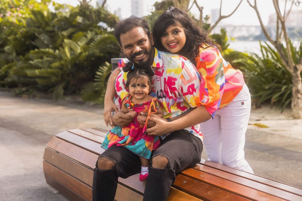 A joyful family wearing colorful floral leis sits together on a wooden bench in a sunny outdoor setting.