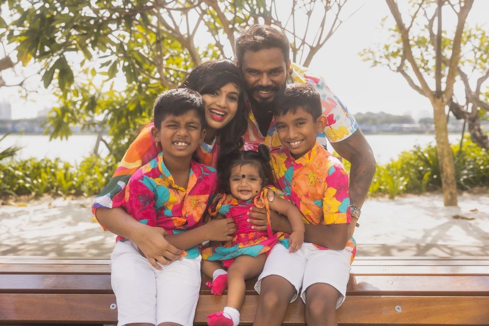 A joyful group wearing bright floral outfits huddle together and laugh while posing for outdoor photos.