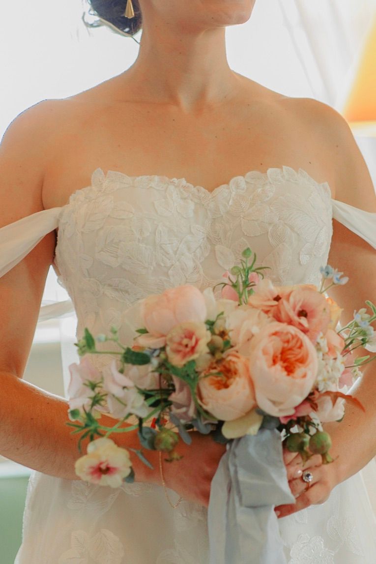A white strapless wedding gown with pink and coral peony bouquet arranged along the neckline in an elegant style.