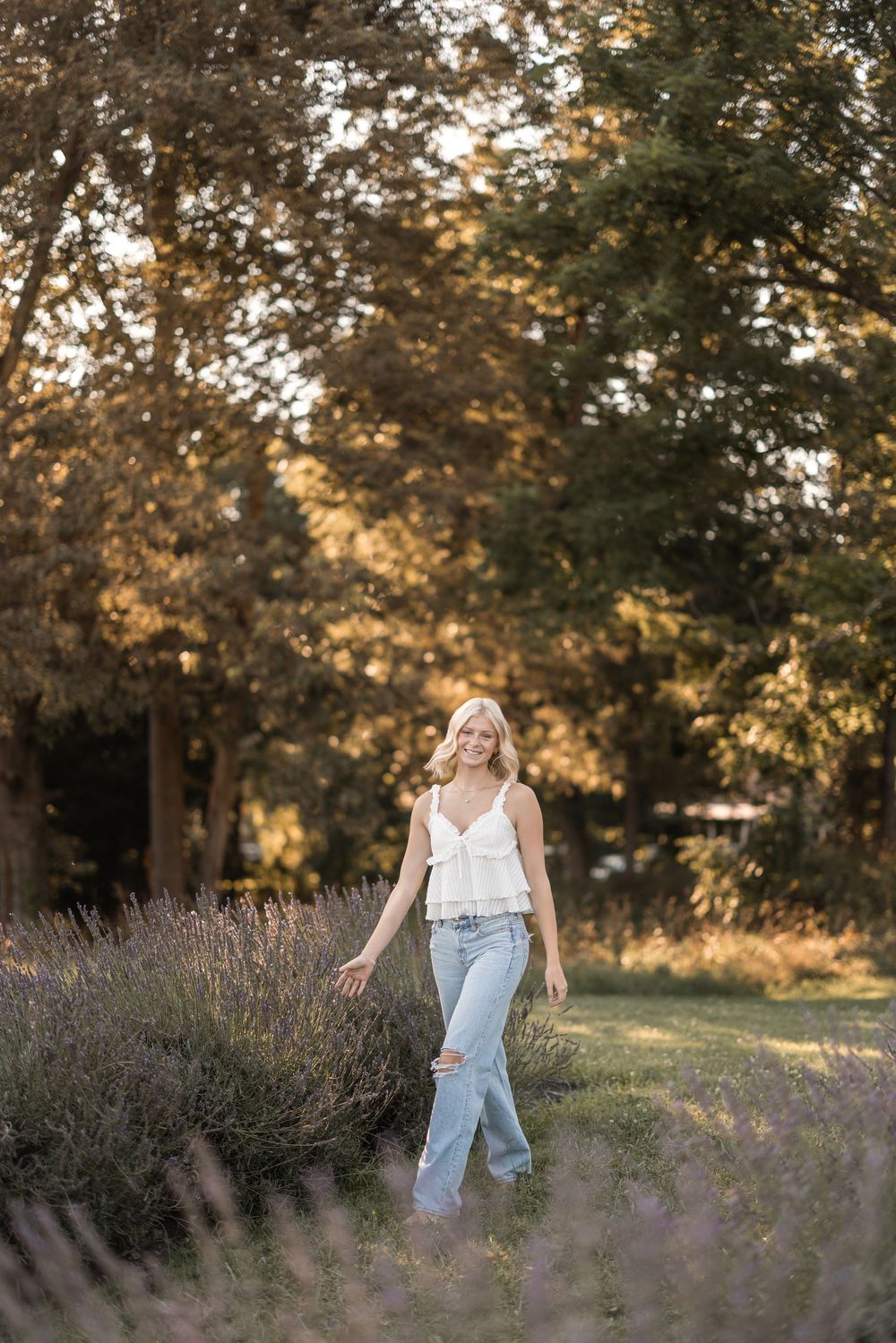 Someone walks through a dreamy meadow at sunset wearing a white tank top and light jeans among purple wildflowers.