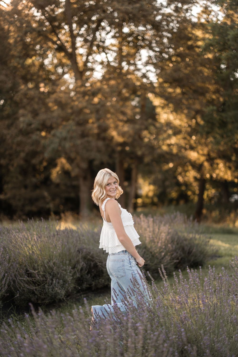 A figure stands amid blooming lavender fields at sunset with warm golden light filtering through trees.