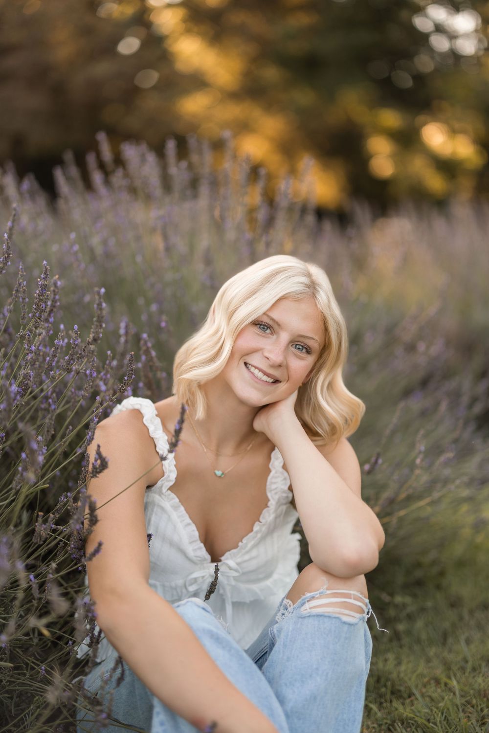 Person in a white top sits amid blooming lavender field during golden hour.