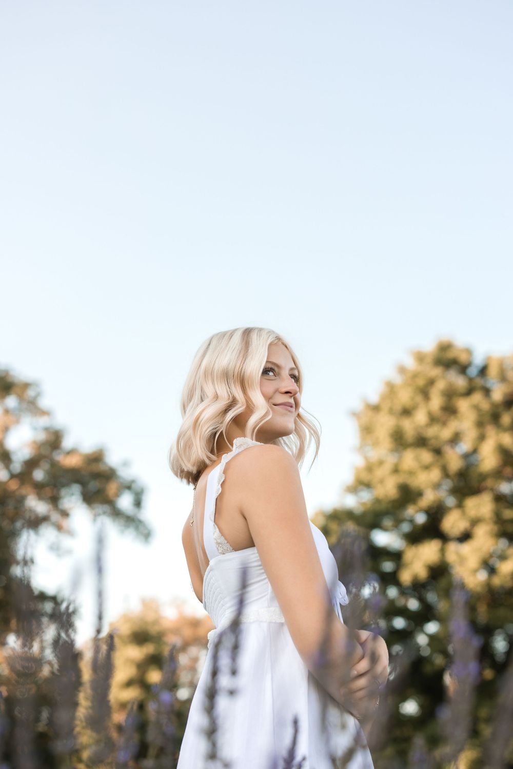Person in white dress poses joyfully against a sun-drenched summer sky backdrop.