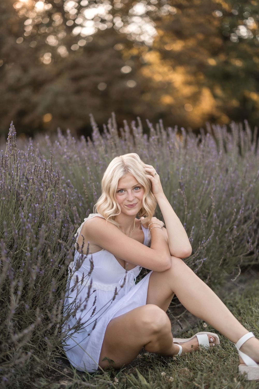 Person relaxing in a field of blooming purple lavender flowers at sunset wearing white attire.