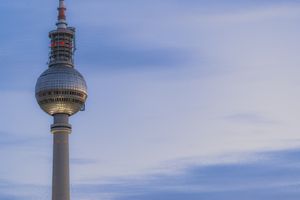 View of the iconic Berlin TV Tower (Fernsehturm) against a blue cloudy sky in Germany.