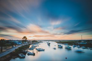 Long exposure sunset over a harbor with boats moored in calm waters and dramatic streaked clouds in the blue sky.