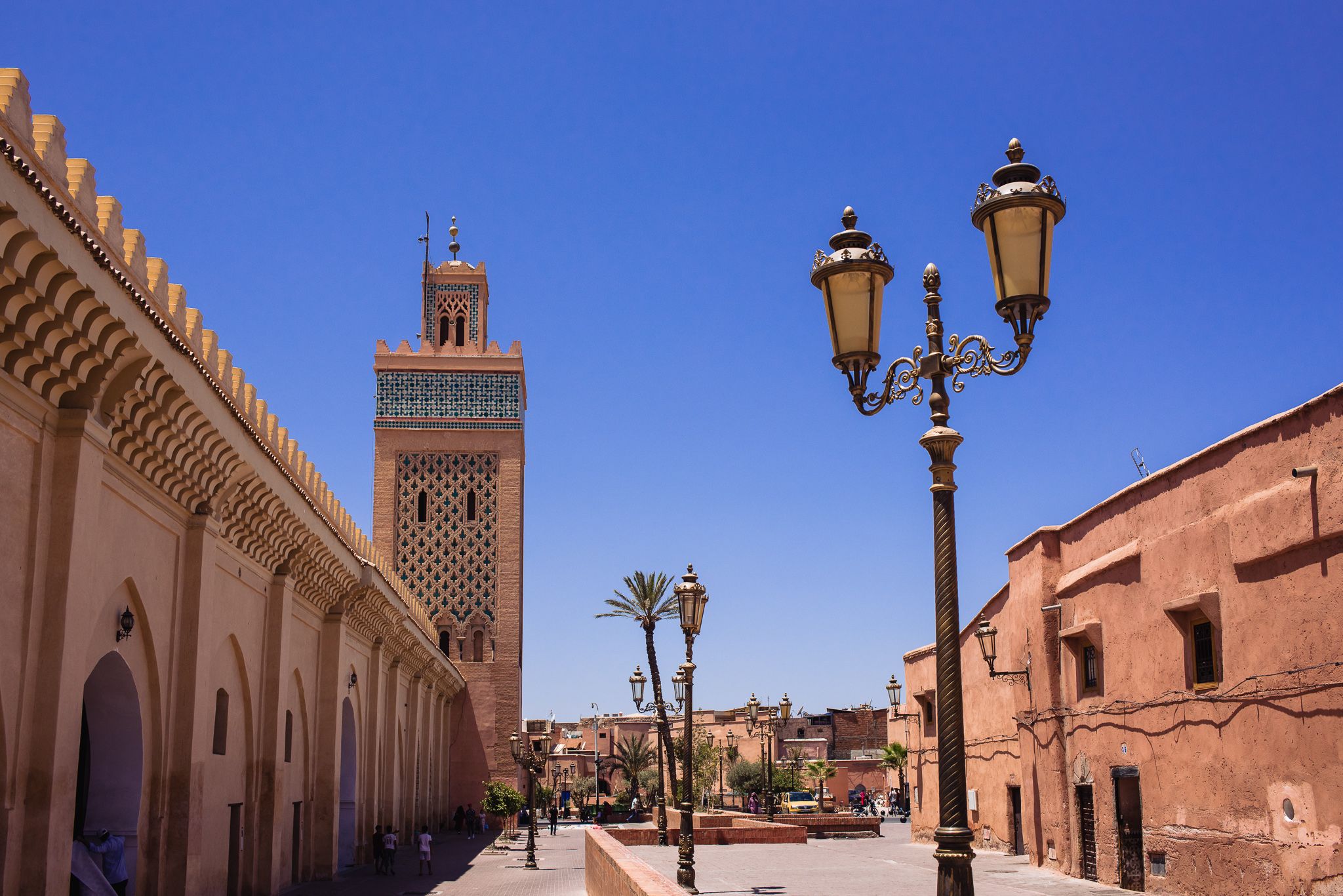 A panoramic view of a historic mosque with terracotta walls and decorative architecture in Marrakech under blue skies.