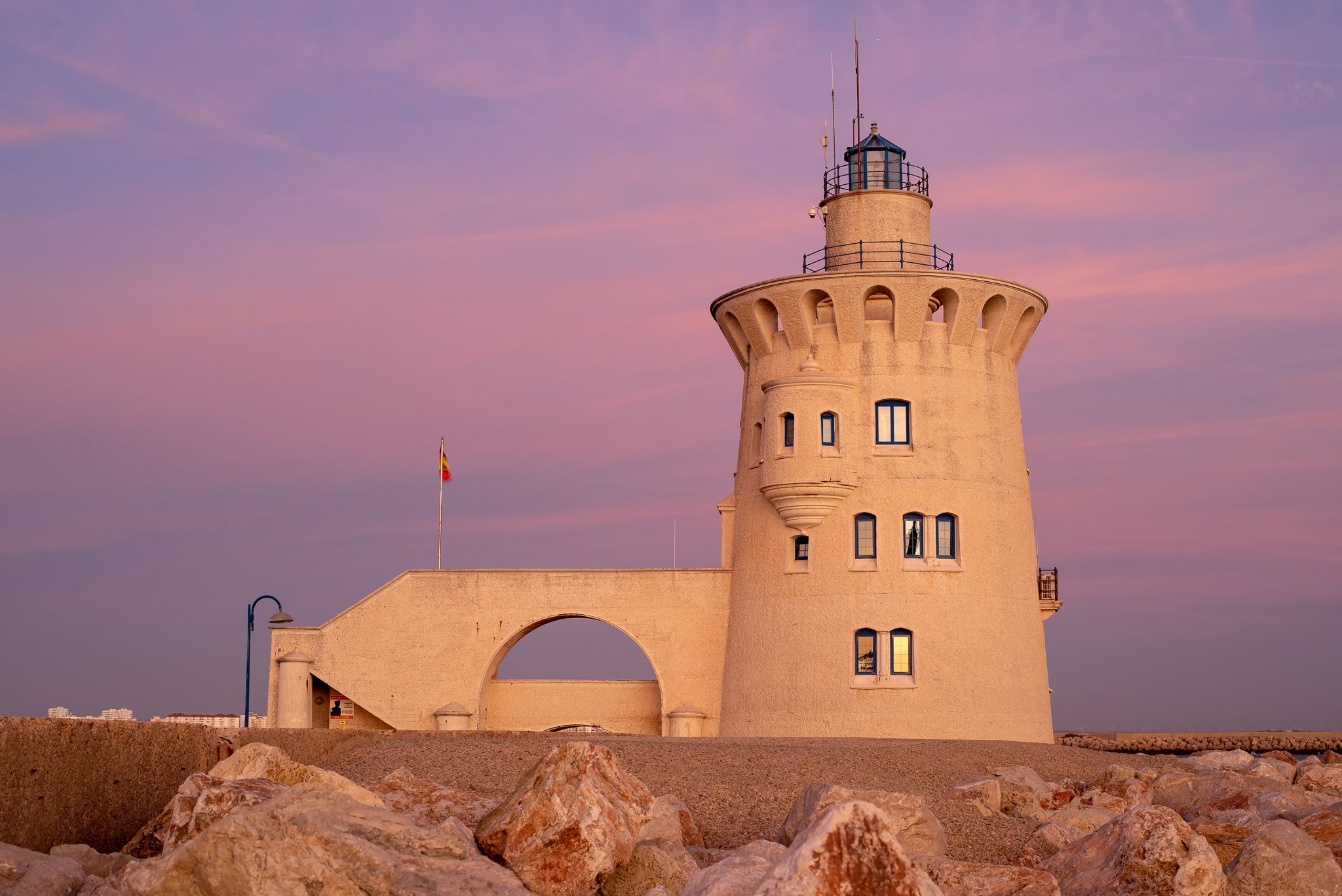 A white lighthouse stands against a purple sunset sky with rocky foreground at South Padre Island, Texas.