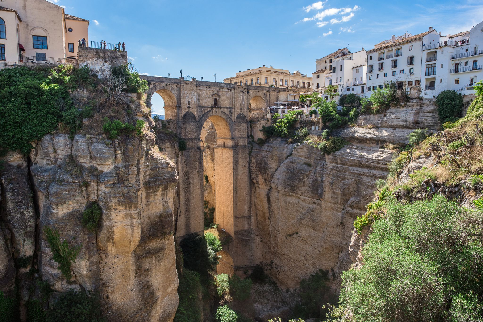 Ancient stone bridge spans dramatic gorge in historic Ronda, Spain with whitewashed buildings perched along cliffs.