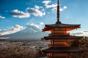 Panoramic view of Mount Fuji with traditional Japanese pagoda and cityscape under blue skies with white clouds.