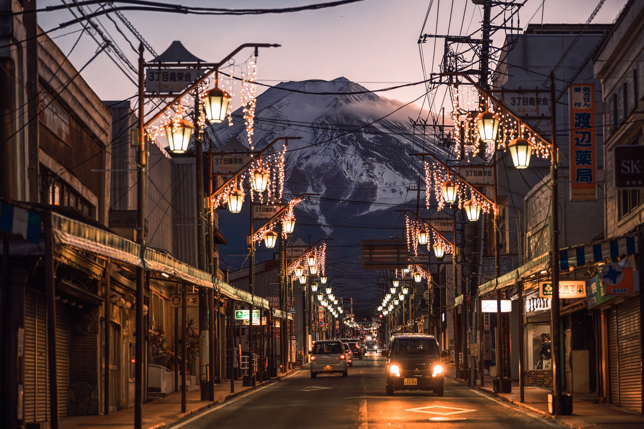 Mount Yotei looms over an illuminated street in Kutchan, Hokkaido during sunset with glowing Japanese lanterns.