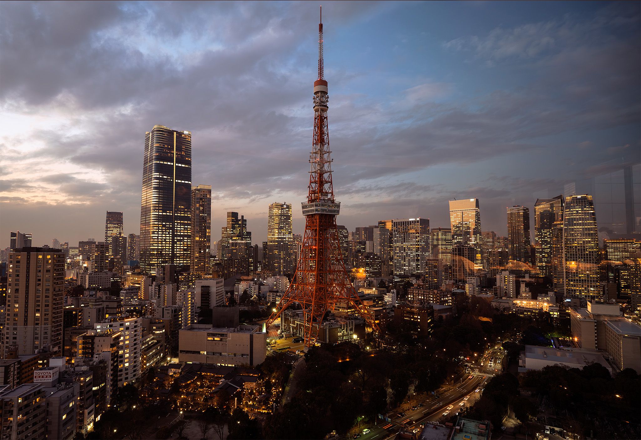 Illuminated Tokyo Tower and city skyline at twilight with dramatic cloudy sky over modern skyscrapers in Japan.