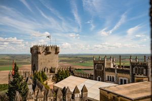 Ancient stone castle walls and towers with battlements stand against a dramatic blue sky with white clouds.