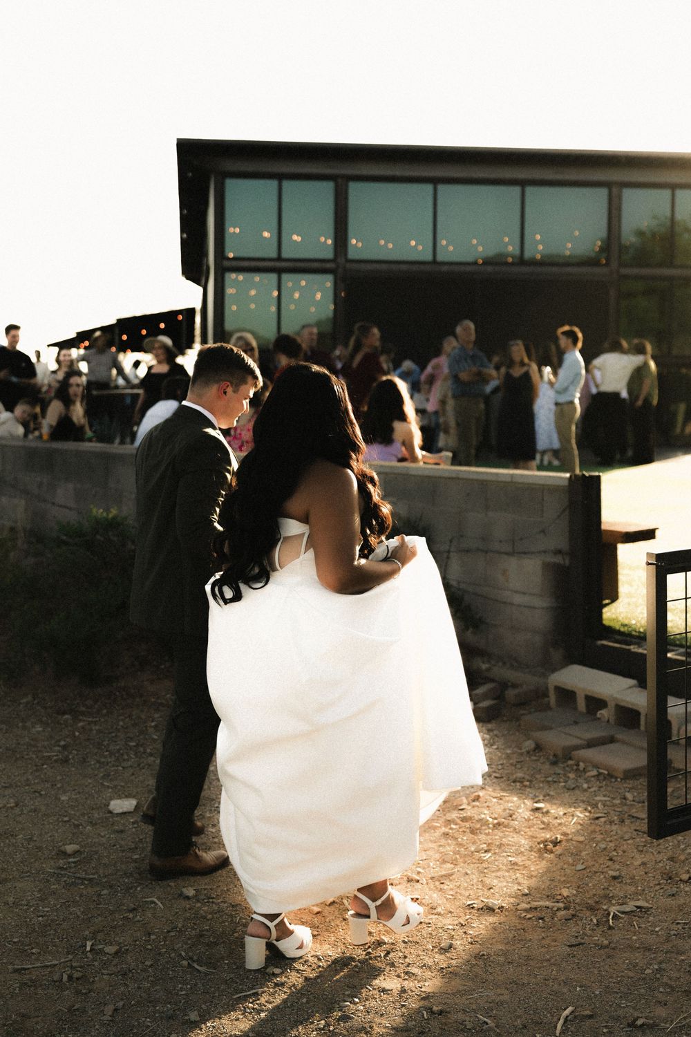Wedding reception silhouettes at sunset with guests gathered outdoors.