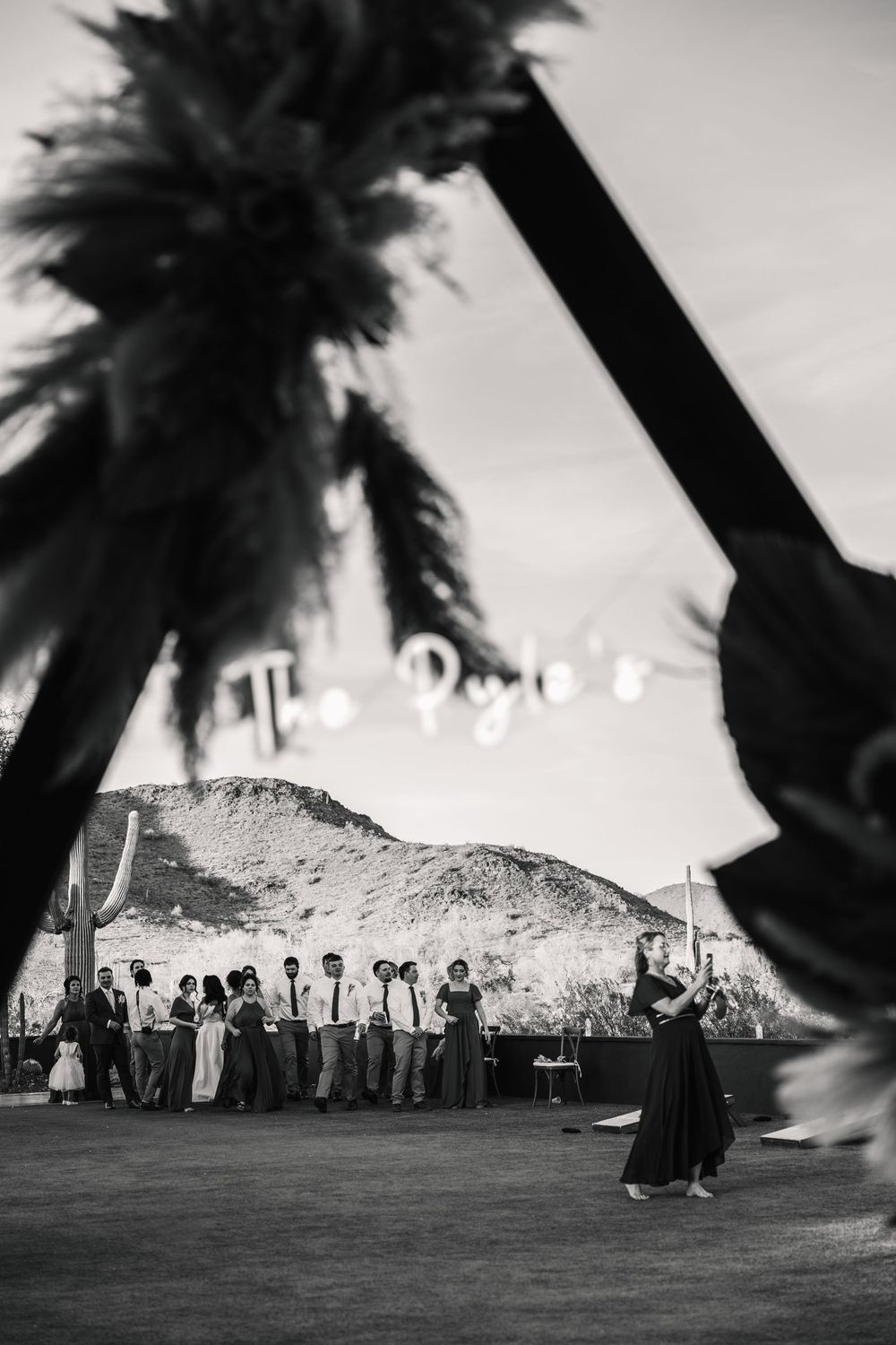 Black and white landscape photo of a wedding celebration with palm trees and mountains.