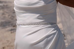 A delicate rhinestone belt adorns the waist of a white wedding dress with elegant fabric draping.