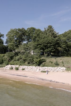 A section of Lake Michigan shoreline with rocks lining the beach and green trees on a bluff above the sandy coastline.