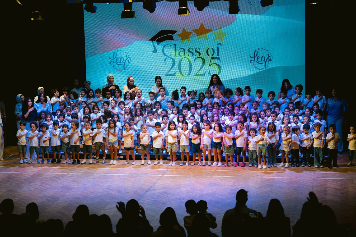Large group of students performing on stage with blue lighting and Class of 2024 projection.