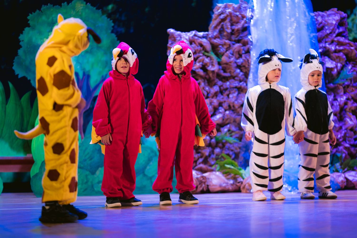 Costumed performers in red and yellow outfits dancing on a blue-lit stage with snowy backdrop.