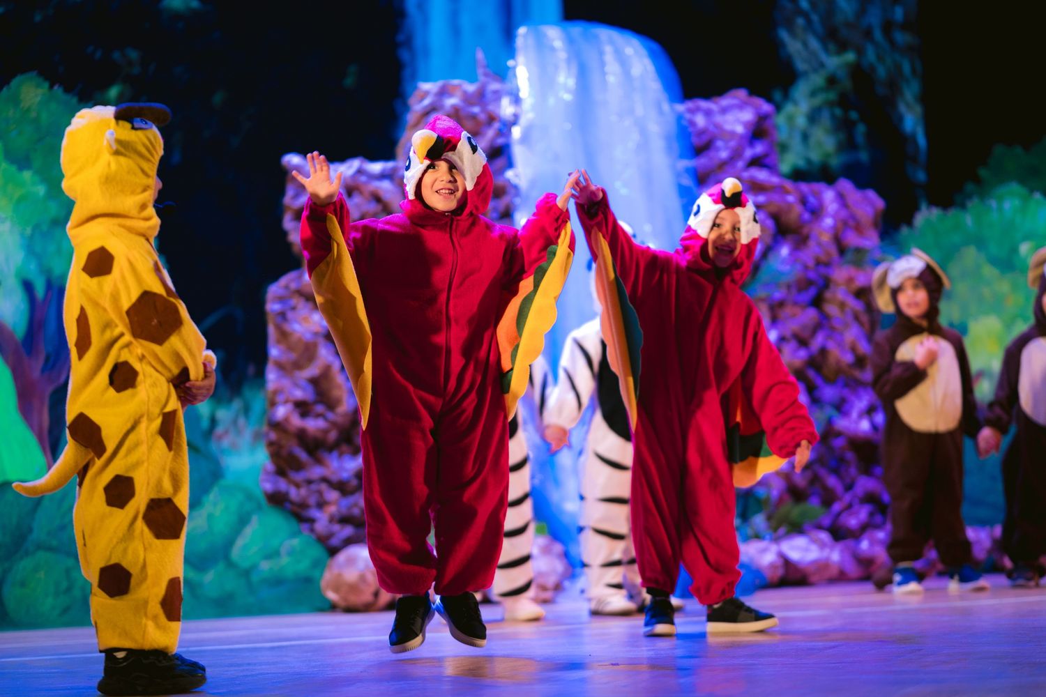 Costumed performers in animal outfits dancing on stage with colorful theatrical lighting.