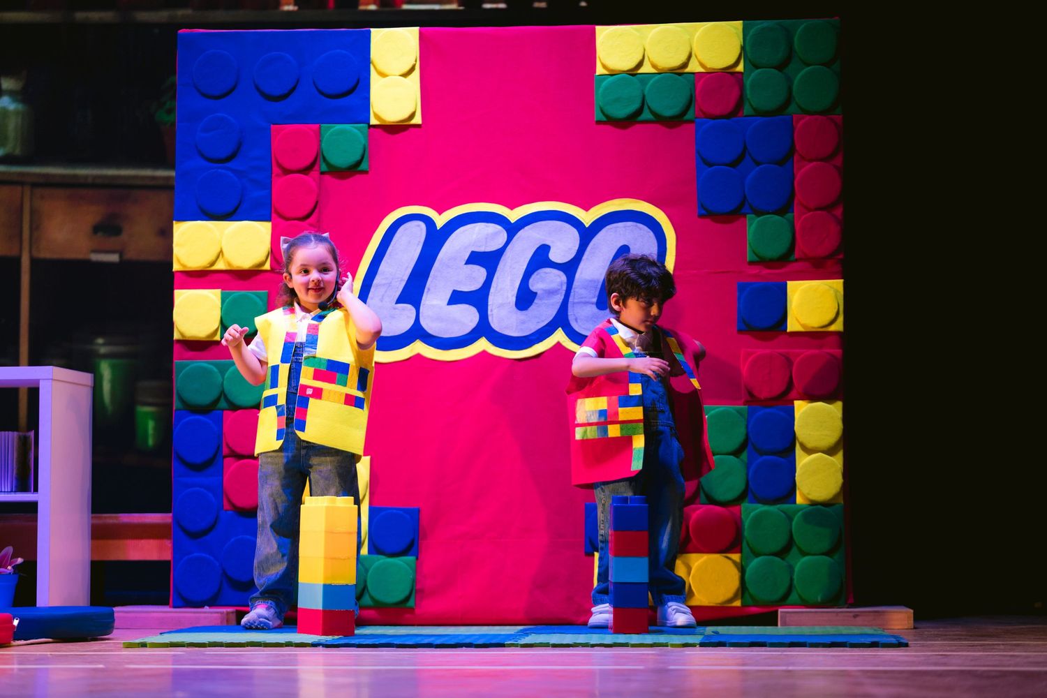 Colorful LEGO-themed stage set with giant building blocks and bright pink background for live performance.