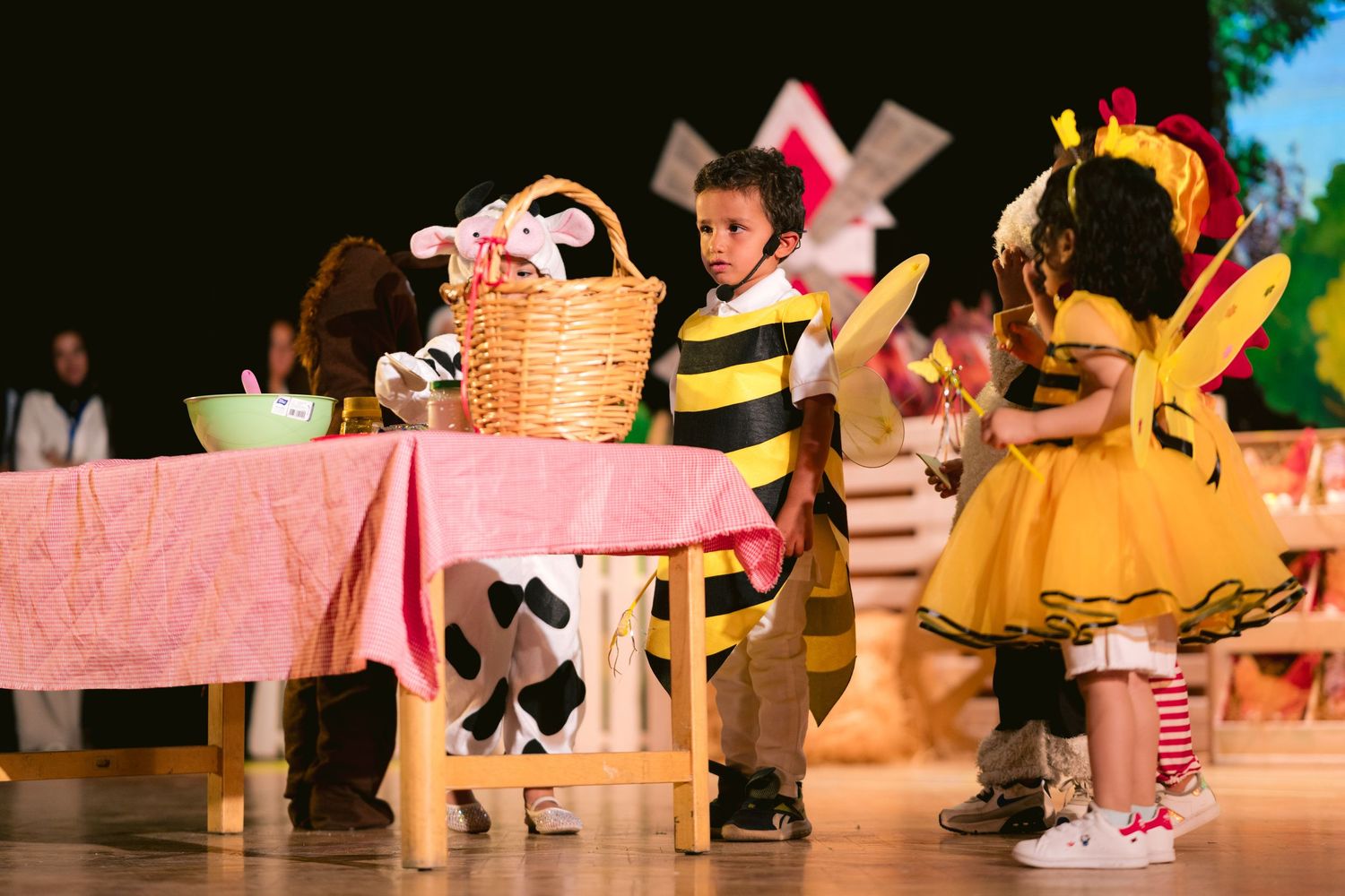 Children perform in a musical theater production with colorful costumes and set pieces on stage.
