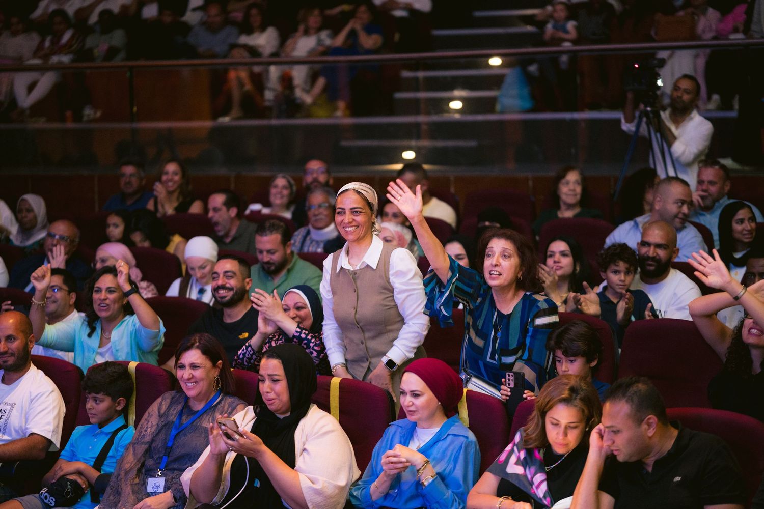 A diverse crowd of engaged audience members watches intently at an indoor event.