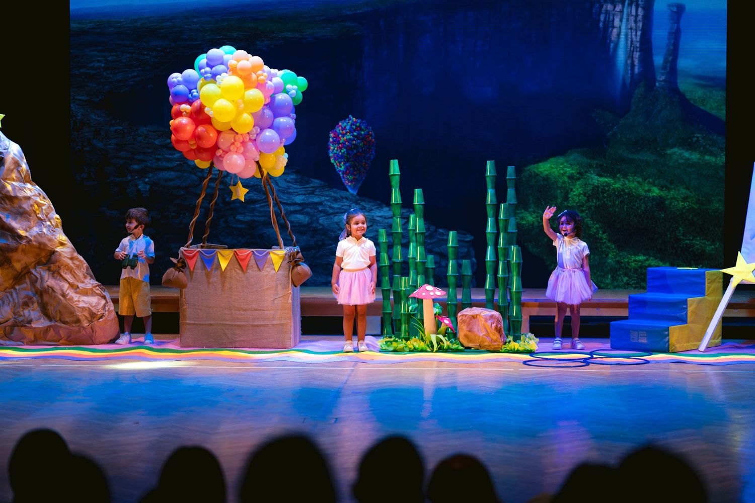 Theater stage with colorful balloon props and performers under dramatic blue lighting.
