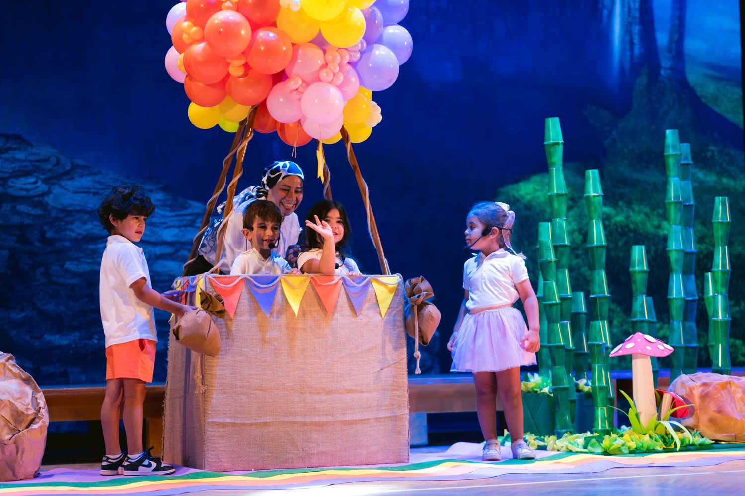 Stage production featuring bright red and yellow balloons against a blue backdrop during a theatrical performance.