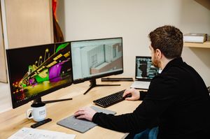 Creative professional working at desk with dual monitor setup showing colorful digital artwork and design software.