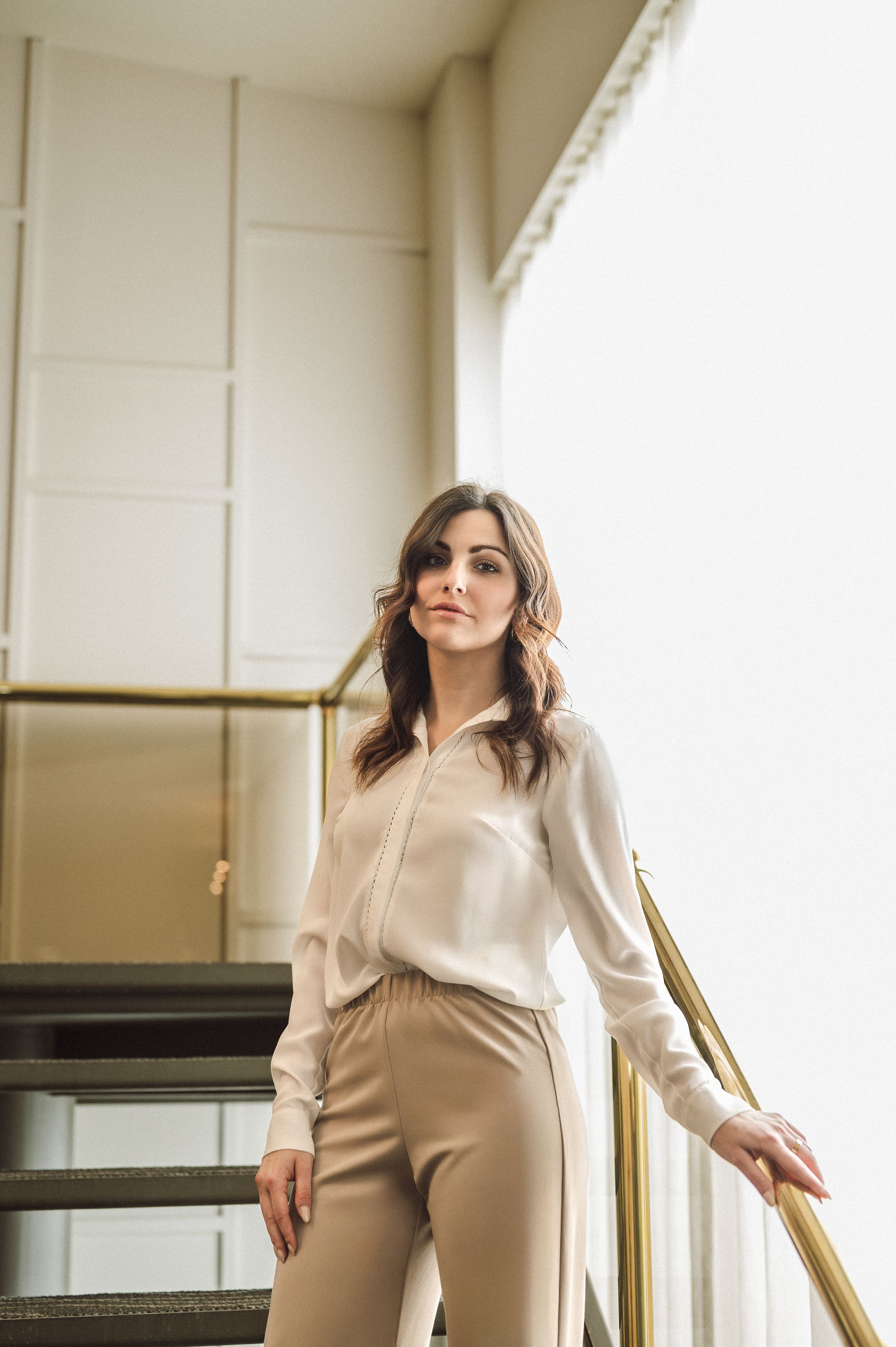 Fashion photoshoot showcasing cream-colored business wear against white interior with metallic accents.