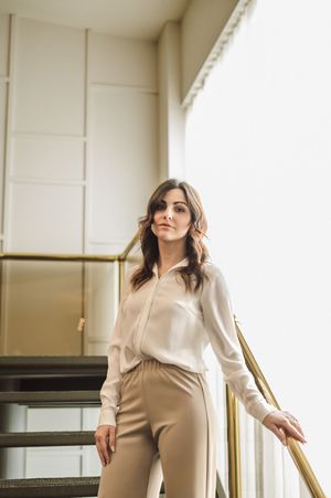 Fashion photoshoot showcasing cream-colored business wear against white interior with metallic accents.