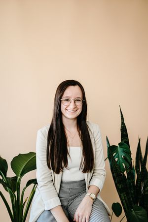 A professional studio portrait against a beige background with indoor plants and modern decor.