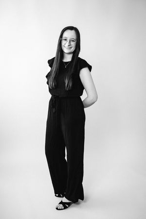 Black and white studio portrait shows a person in a flowing sleeveless dress standing against a white backdrop.